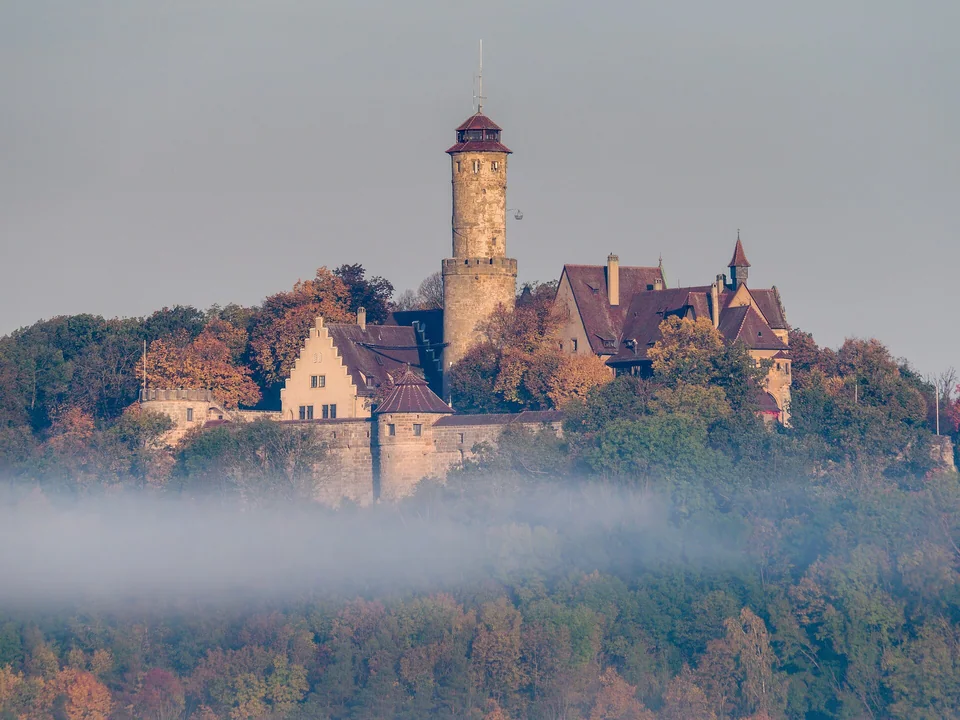 Die Altenburg im Herbstnebel – Die Burg ragt über ein zartes Nebelband und herbstliche Baumkronen.