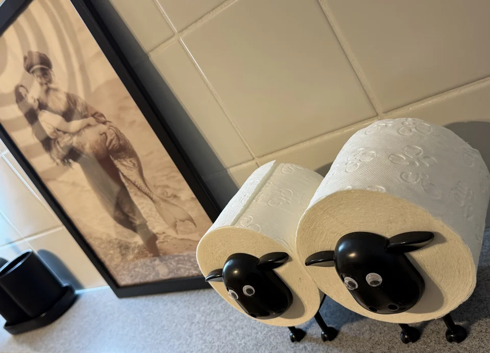 Zwei Schaffiguren halten Papierrollen auf der Ablage im Badezimmer. – Apartment Mittendrin.