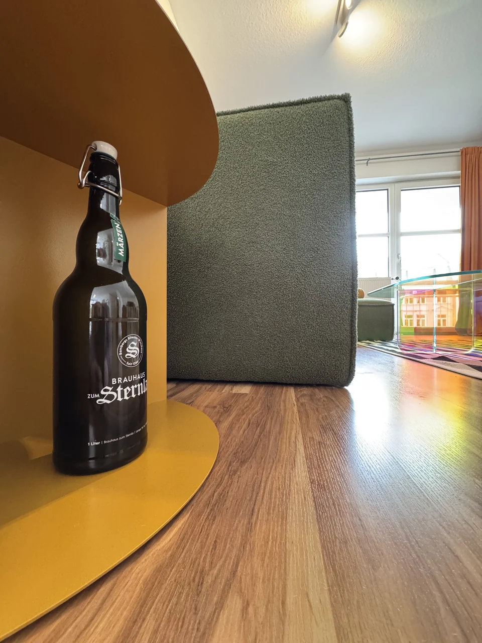 Eine dunkle Bügelflasche am gelben Beistelltisch neben dem Sofa. – Apartment Mittendrin.