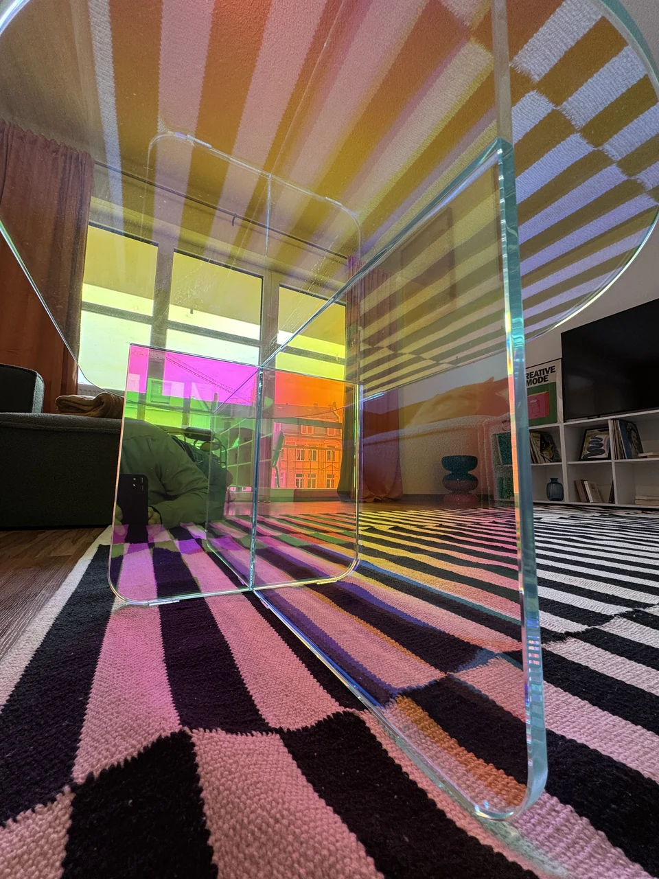 Transparenter Beistelltisch mit farbigen Reflexionen auf dem geometrisch gemusterten Teppich. – Apartment Mittendrin.
